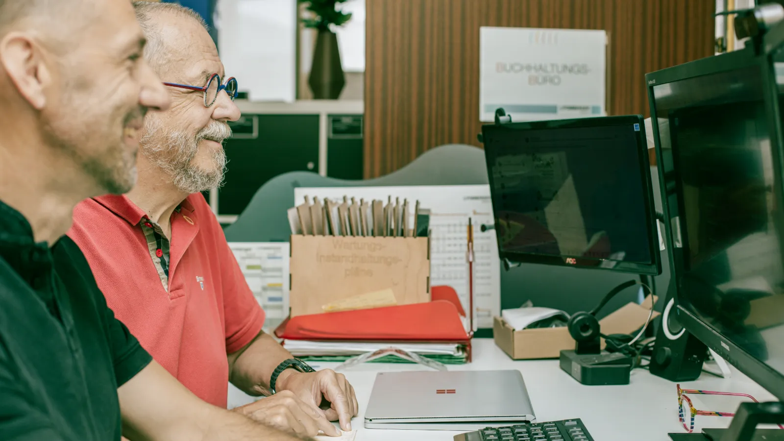 Zwei Kollegen lachen gemeinsam am Bildschirm im Büro